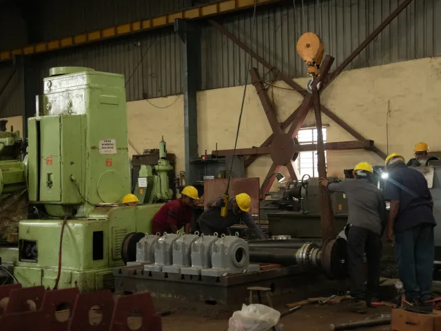 Workers handling a large metal component beside a machine.