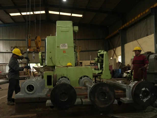 Workshop machinery and heavy metal components with workers nearby.