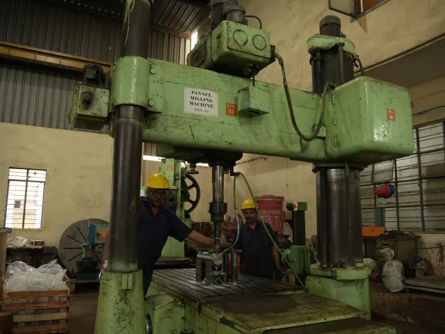 Two workers beside a large green machine tool.